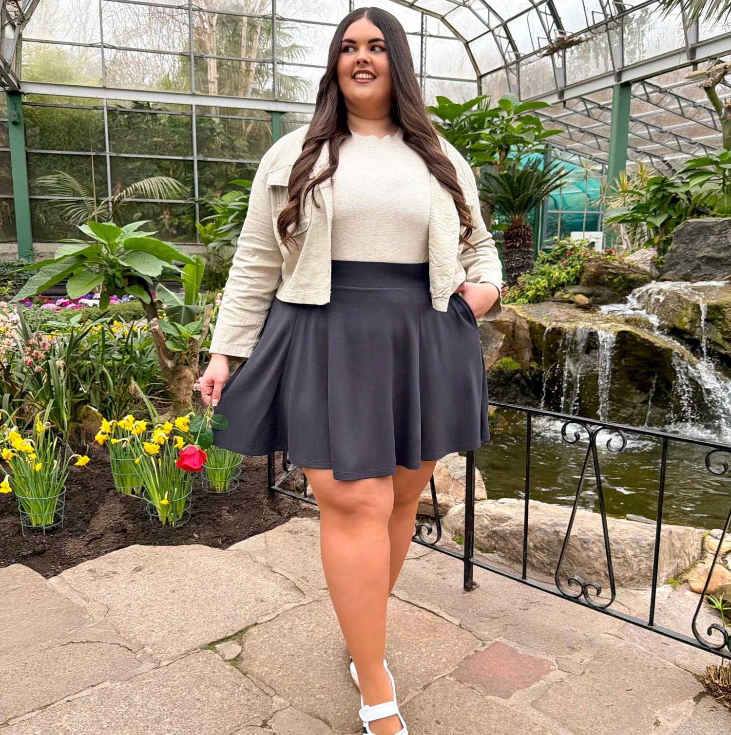 Woman in a garden setting wearing a white jacket and dark gray skirt.